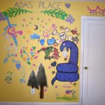 Photo of painted mural inside Ada's house in Columbus, OH. Includes a large snake, trans flag, trees, flowers, and "titties".