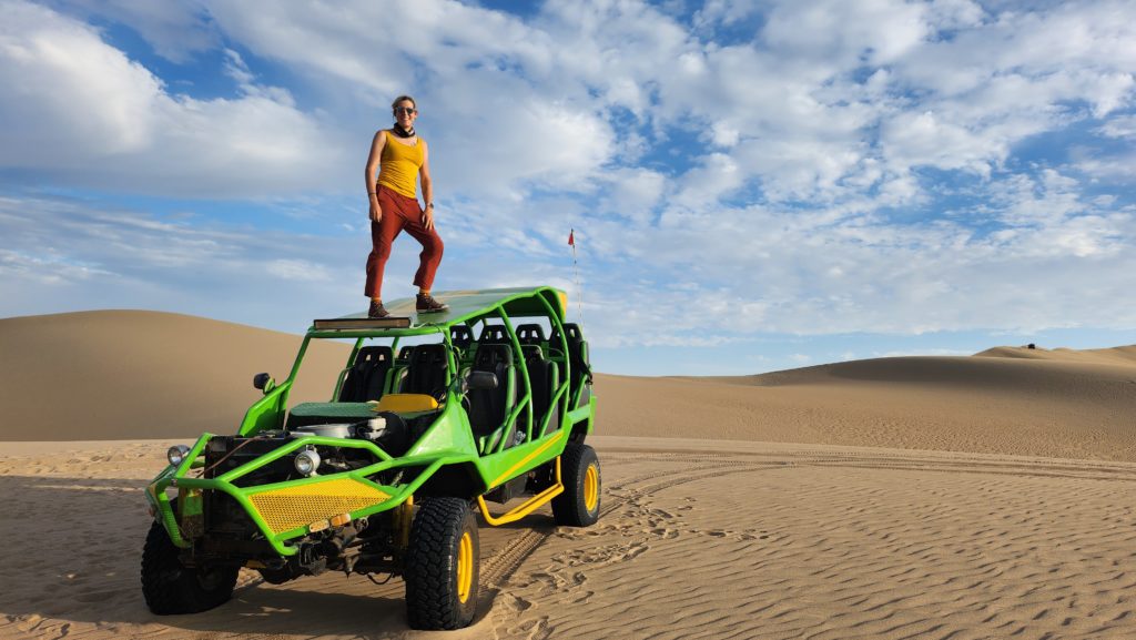 Ada standing on top of a green dune buggy parked in the middle of the desert.