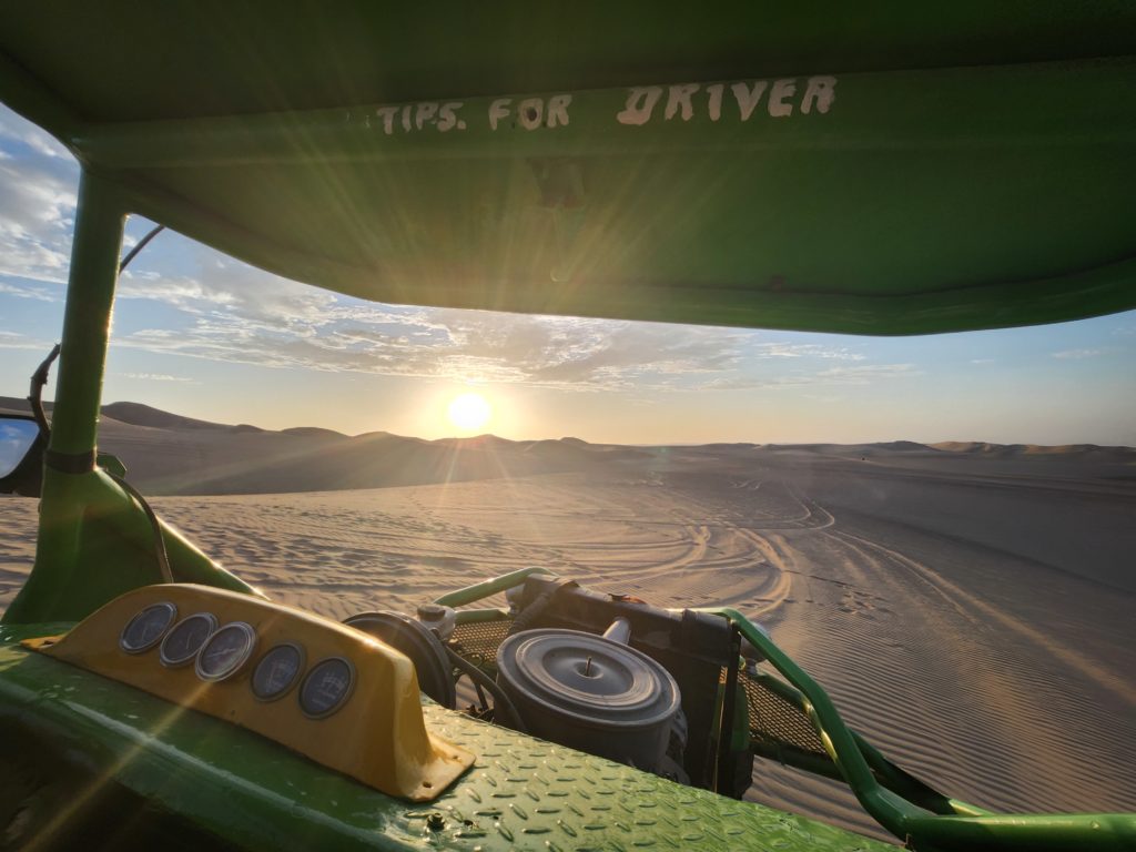 Photograph of a desert landscape at sunset, taken from the inside of a lime-green and yellow dune buggie.