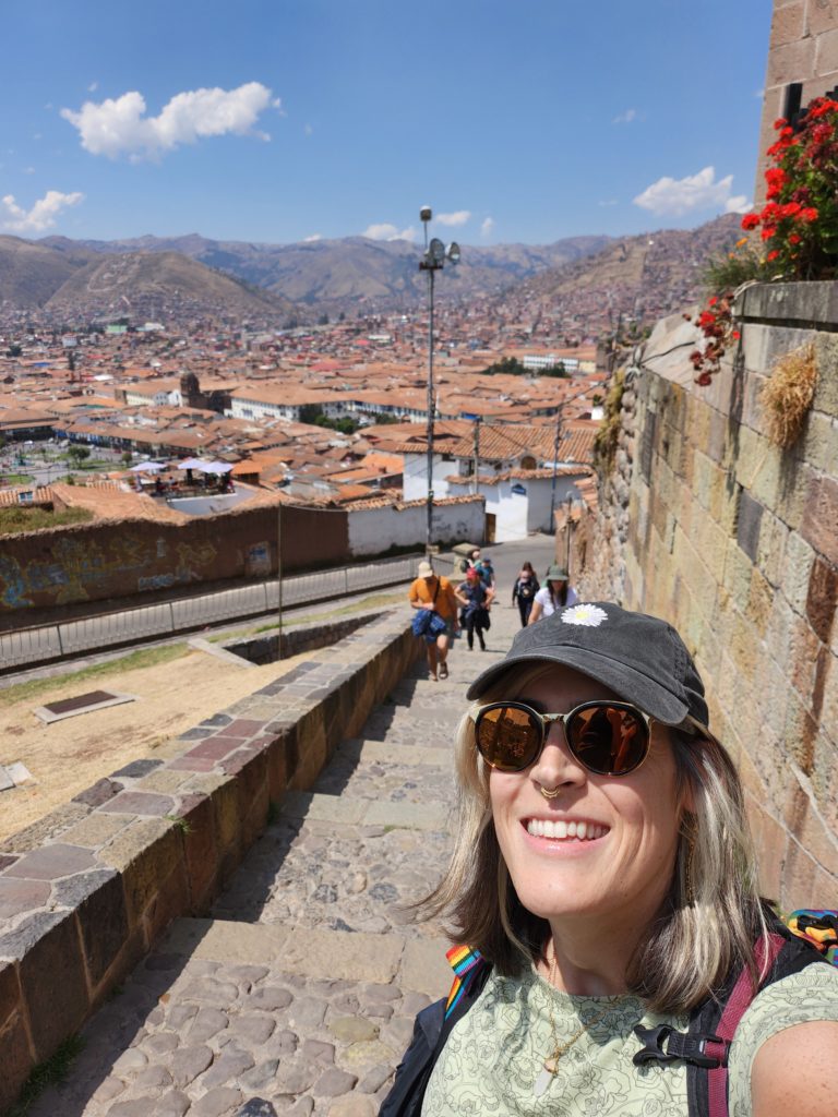 Selfie of Ada on a staircase, with members of their travel group and the city of Cusco, Peru in the background.