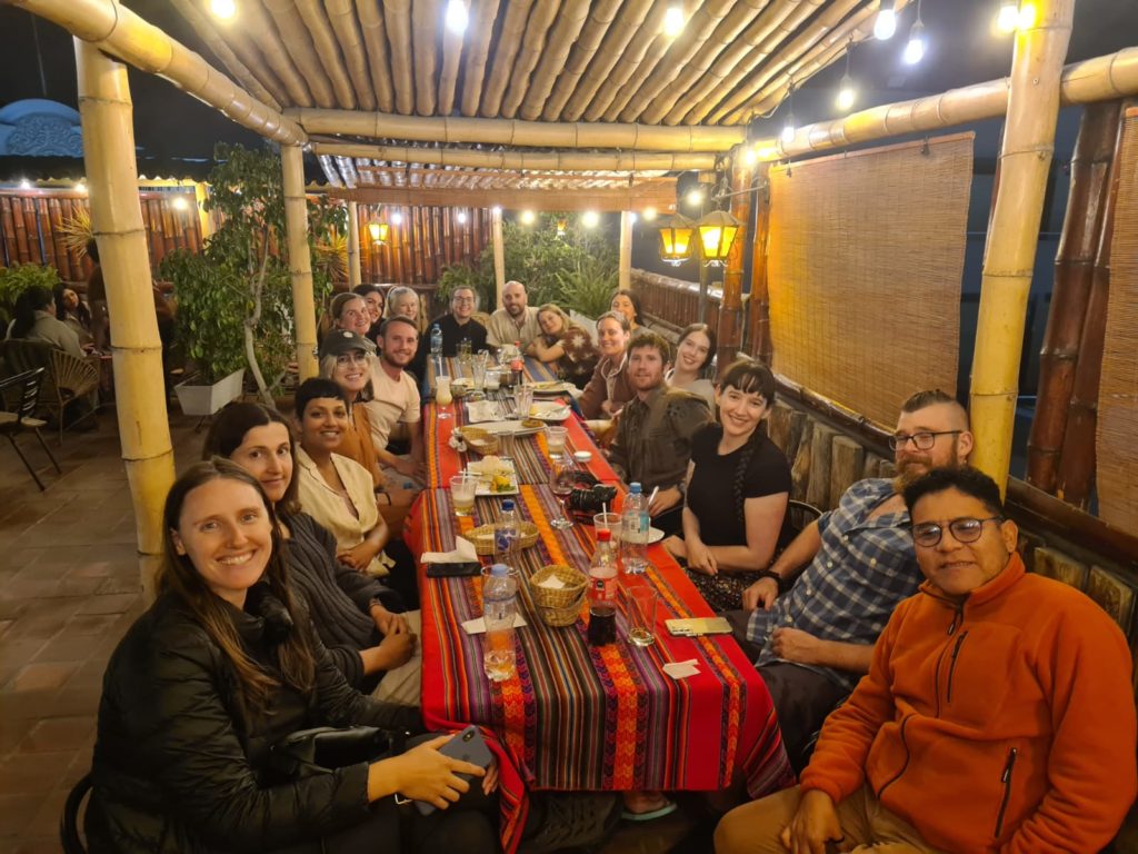 Photo of Ada's Peru travel group around a long dinner table draped in a colorful tablecloth.