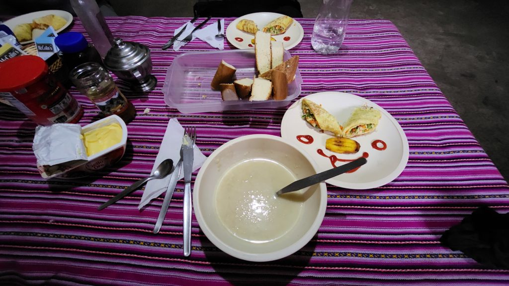 Photo of a breakfast spread on a colorful tablecloth, including porridge and a fried-banana dish plated in the shape of a smiley face.