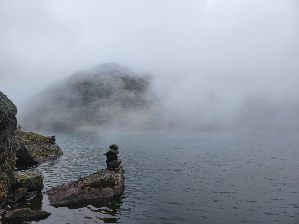 Photo of a lagoon with rocky shores, partially clouded in fog.