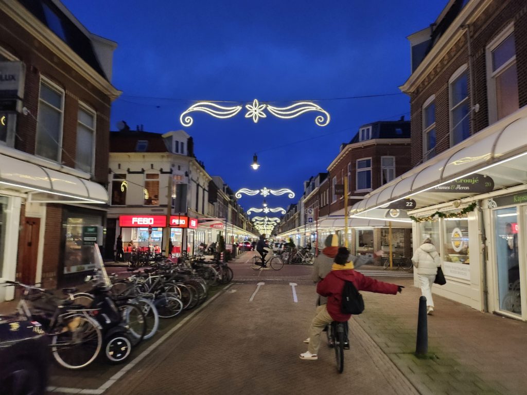 Photo of Cronjestraat, a shopping street in Haarlem. It is nighttime and there are white christmas lights over the street.