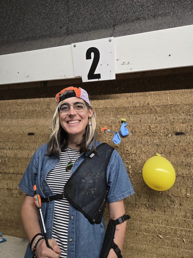 Photo of Ada in front of an archery target with popped balloons.