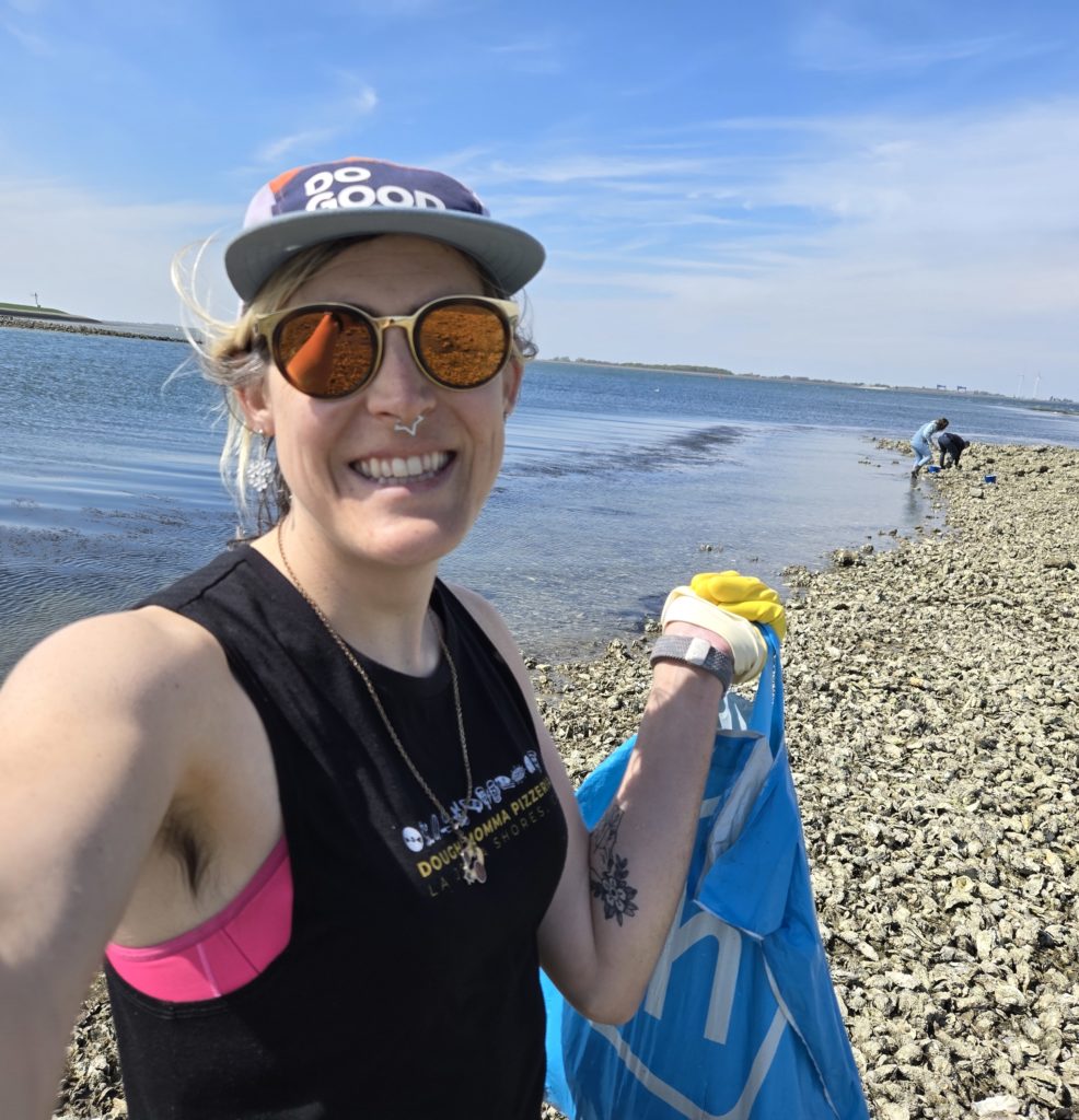 Photo of Ada on a rocky beach, holding a plastic bag full of freshly-harvested oysters